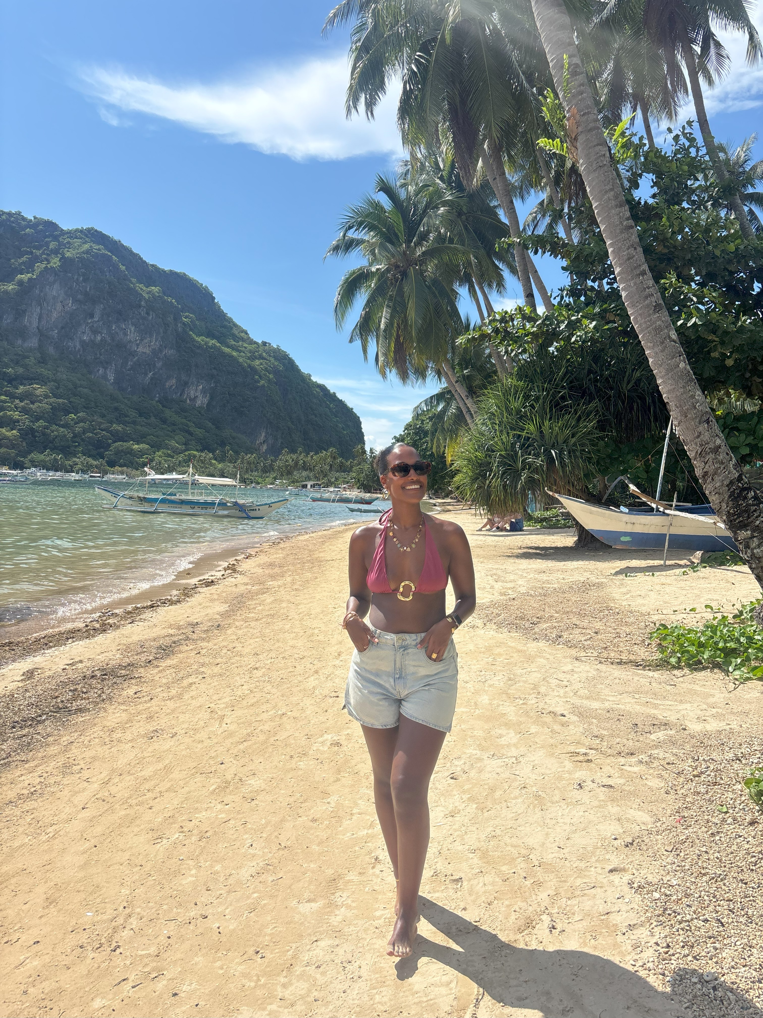 Kvindelige rejsende i shorts og bikinitop på en strand i Filippinerne. 