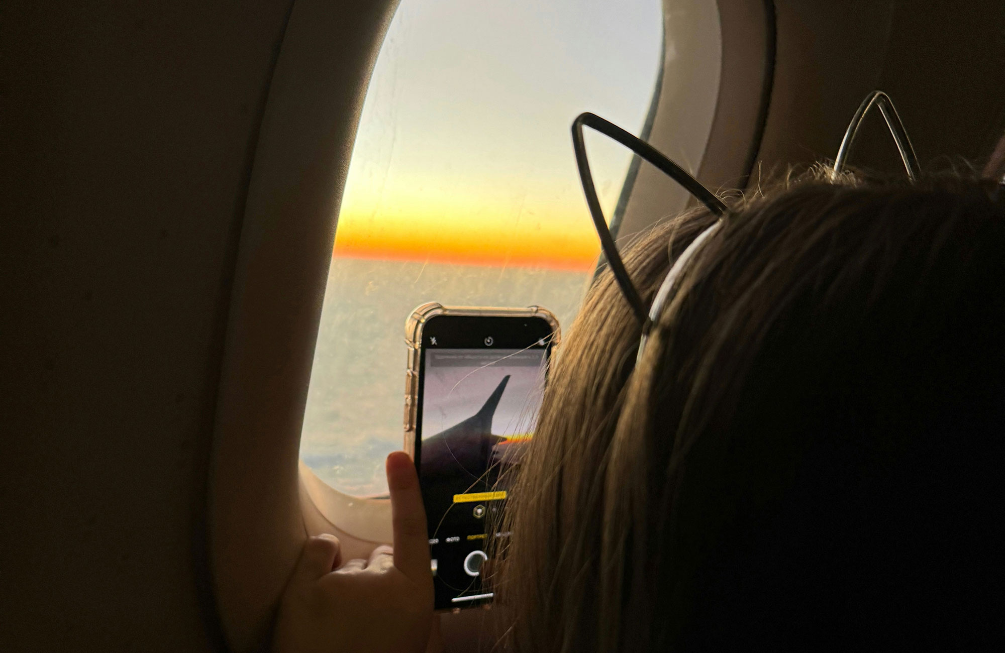 En jente med katteører som filmer ut av et flyvindu. Foto.